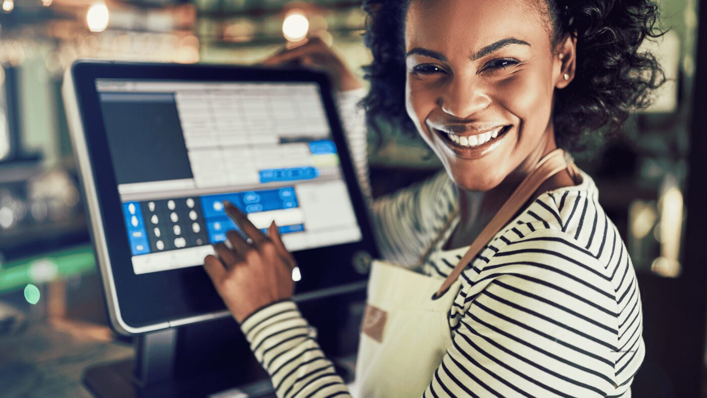 Smiling shop employee ringing up a sale on a point-of-sale tablet