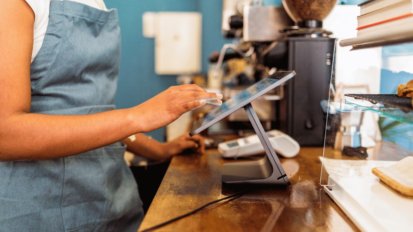 Close-up of a hand tapping a point-of-sale tablet screen at a checkout counter